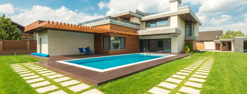 A modern luxury home featuring a backyard swimming pool and wooden decking. A valid Pool Safety Certificate QLD is required for such properties to ensure fences and barriers meet current safety legislation.